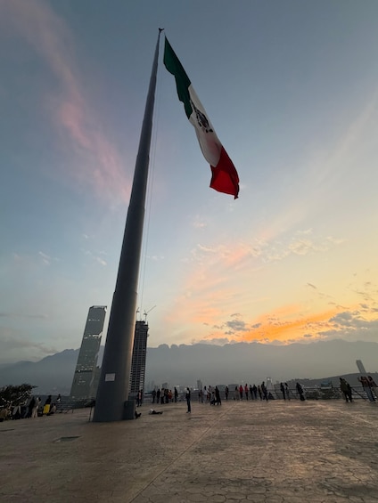 A tall flagpole with a flag, a modern building, and a crowd of people. 4