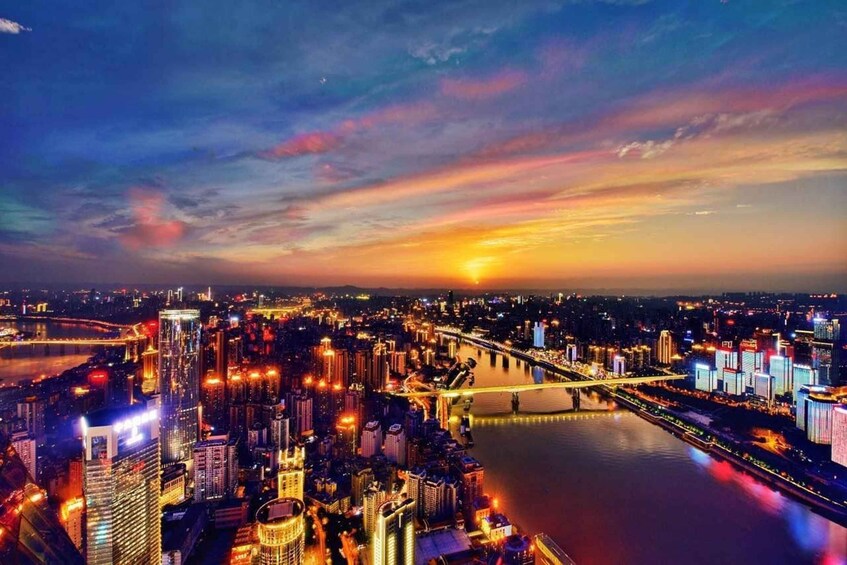 A cityscape at dusk with illuminated buildings, a river, and a bridge. 2
