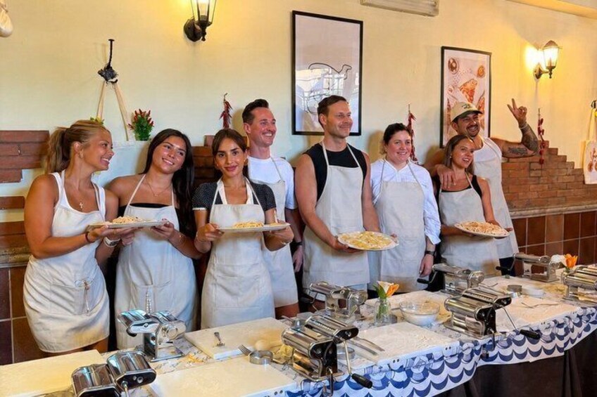 A group of people in aprons holding plates of food in a kitchen setting. 1