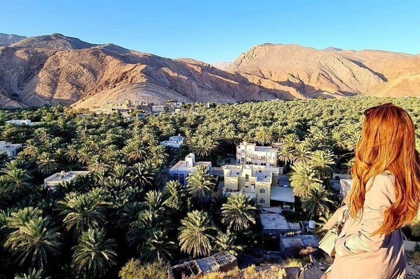 A woman overlooking a village with palm trees and mountains in the background. 5