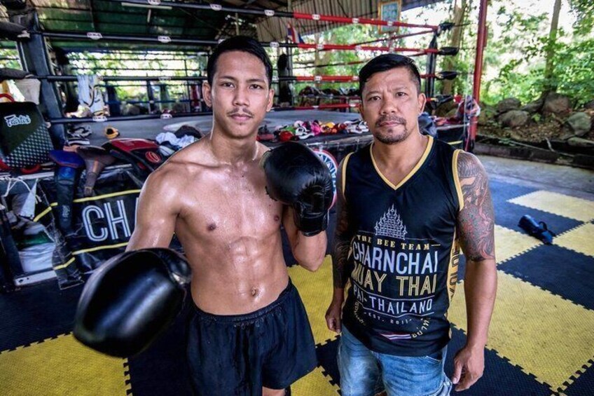 Two individuals in a gym with boxing gloves, a punching bag, and various training equipment. 3