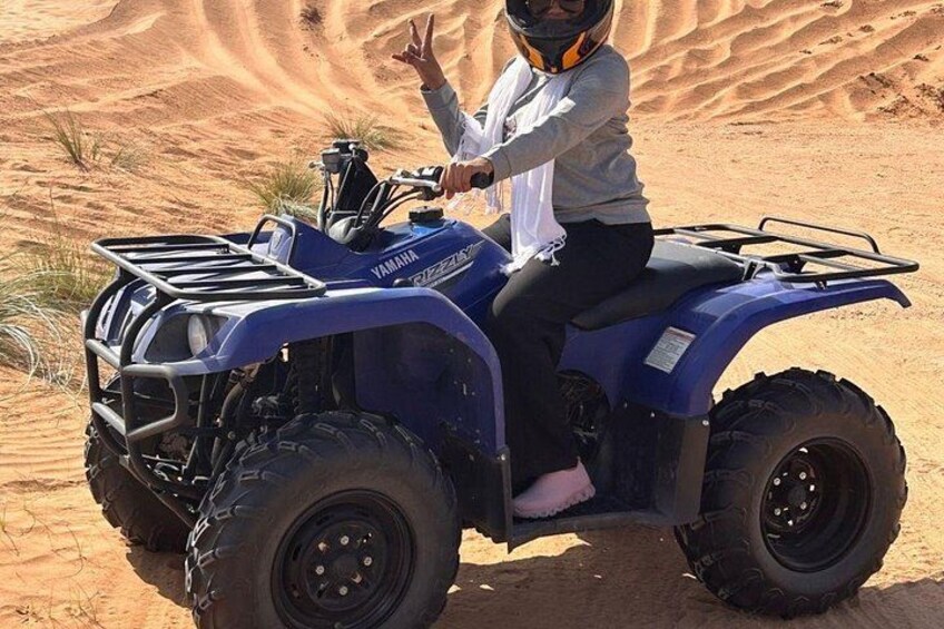 A person riding a blue Yamaha ATV in a desert with sand dunes in the background. 3