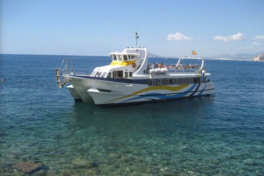 A white and blue boat with 'Super Vision' written on it, floating on clear blue water with a mountainous landscape in the background. 1