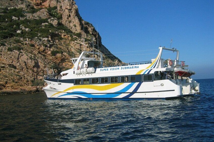 A white and blue boat named 'Super Vision Submarine' on calm water near rocky cliffs. 3