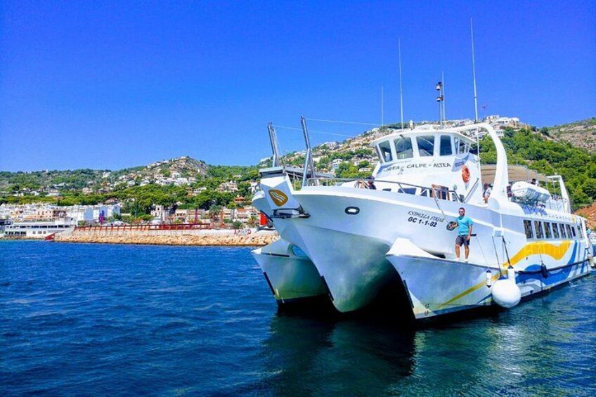 A boat with the name 'Calpe - Atea' docked at a harbor with a coastal town in the background. 2