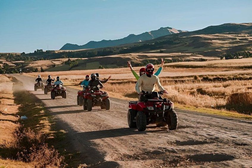 A group of people riding ATVs on a dirt road in a rural landscape with rolling hills and clear skies. 1