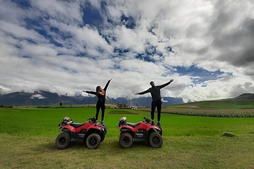Two people standing on red ATVs in a grassy field with mountains in the background. 5