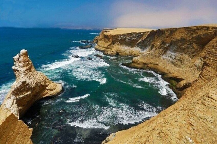 A coastal cliff with a prominent rock formation, ocean waves crashing against the shore, and a clear sky. 1
