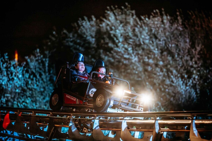 A nighttime roller coaster ride with two passengers, illuminated headlights, and a blurred background of trees. 4