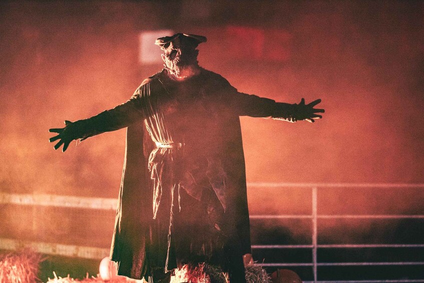 A person in a long robe with outstretched arms, standing in a dimly lit area with a red hue. 2
