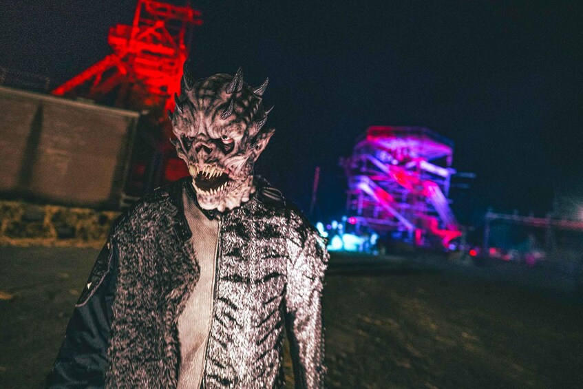 A person in a textured jacket standing in front of a construction site with a red crane and a lit-up structure in the background. 5