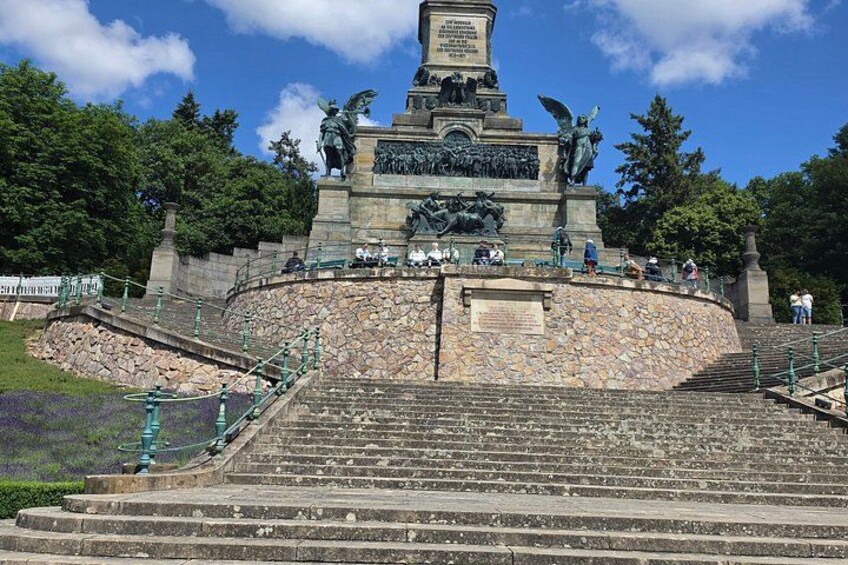 A monument with a statue at the top, surrounded by stone steps and greenery. 1