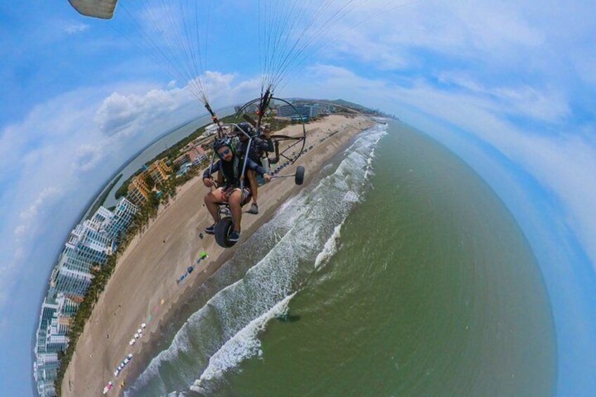 A person paragliding over a beach with buildings in the background. 1
