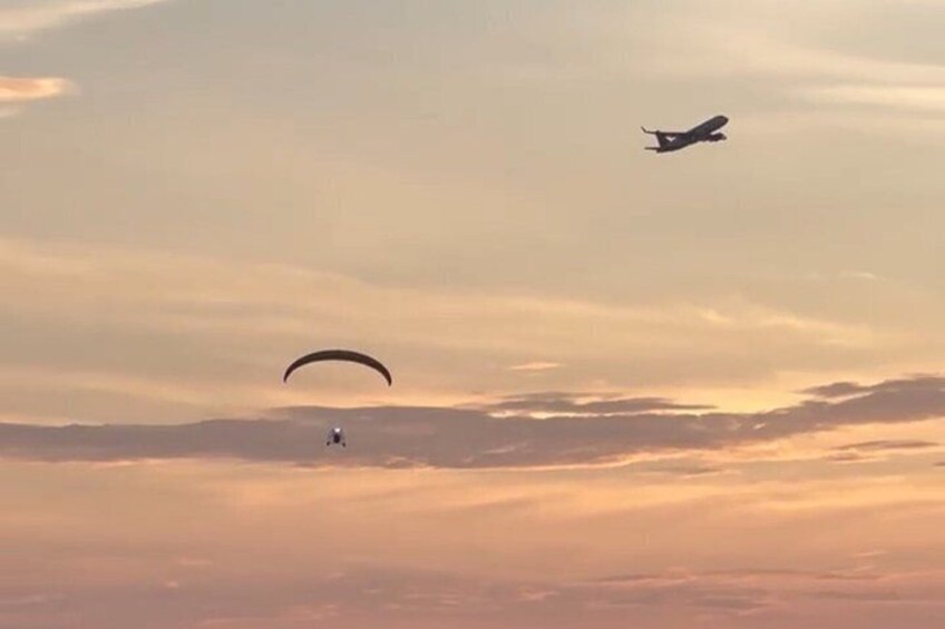 A paraglider and an airplane in the sky during sunset. 3