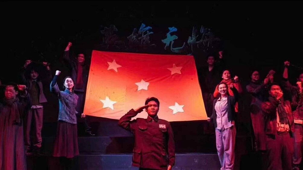 A group of people on a stage with a large flag, some saluting, and others raising their hands. 2