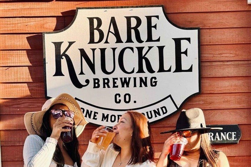 A sign for Bare Knuckle Brewing Co. with three people drinking. 4