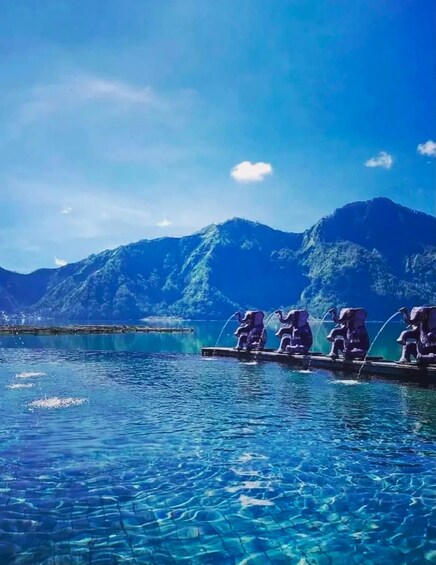 A clear blue lake with mountains in the background and a row of elephant statues on a dock. 3
