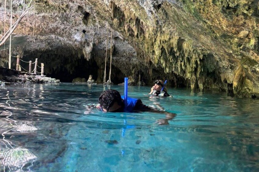 A person snorkeling in a clear blue pool with rocky cave walls in the background. 5