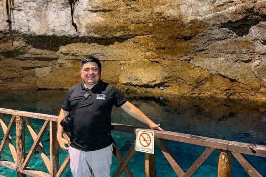 A person standing on a wooden bridge over a clear blue pool with a cave wall in the background. 4