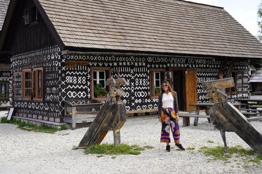 A traditional wooden house with intricate patterns, a person in colorful attire, and wooden sculptures. 5