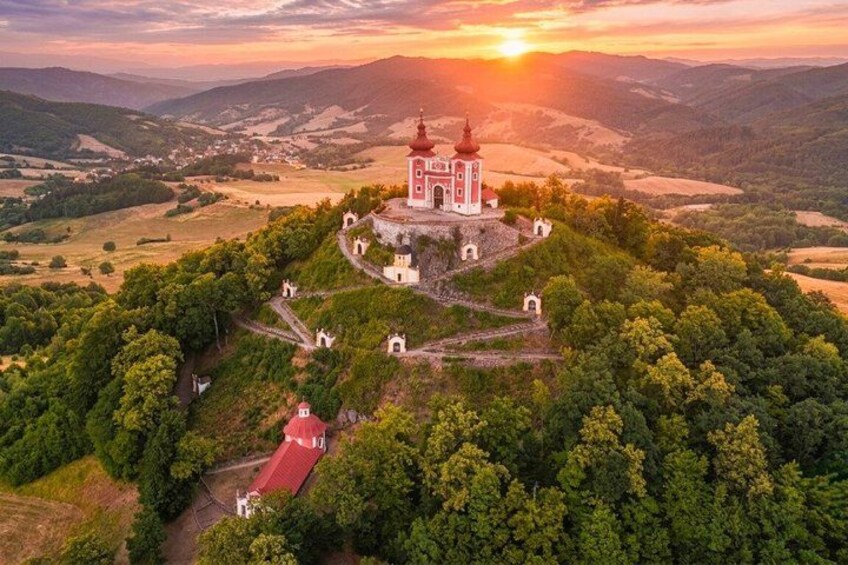 A church on a hilltop surrounded by forest, with a sunset in the background. 3