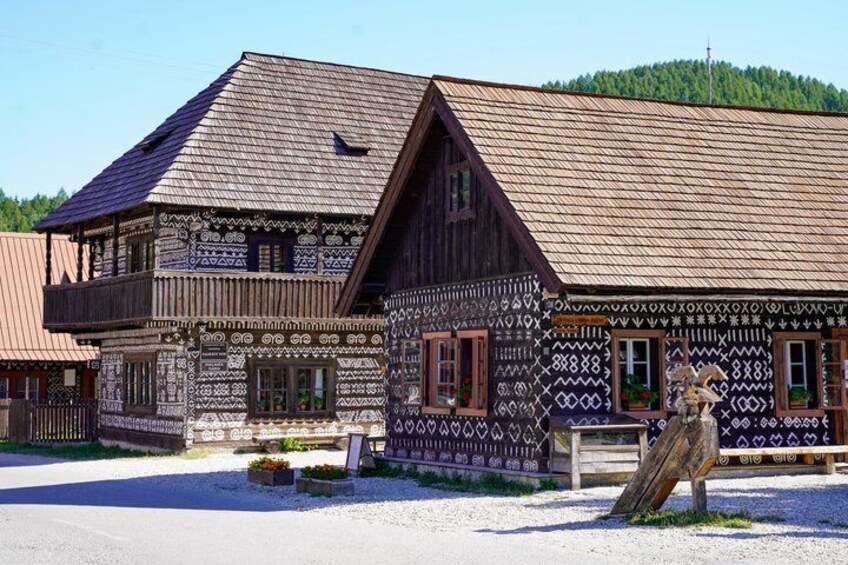 A traditional wooden house with intricate patterns, a balcony, and a statue in front. 3