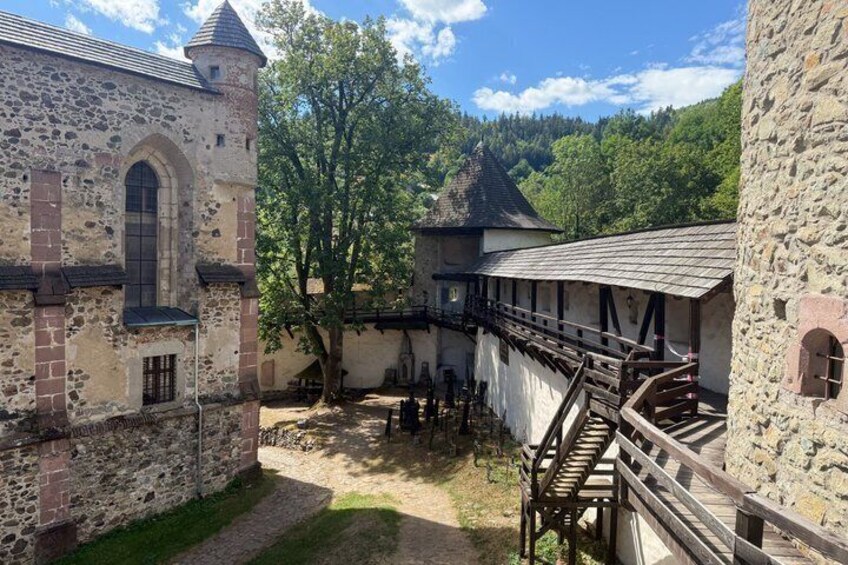 A historic stone building with a tower, a wooden bridge, and a tree in a courtyard. 4