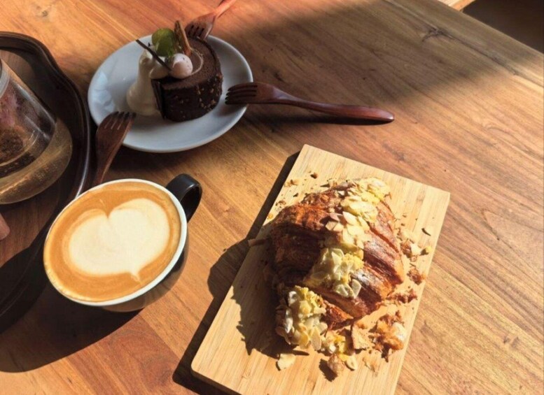 A wooden table with a croissant, a plate with a dessert, and a cup of coffee. 3