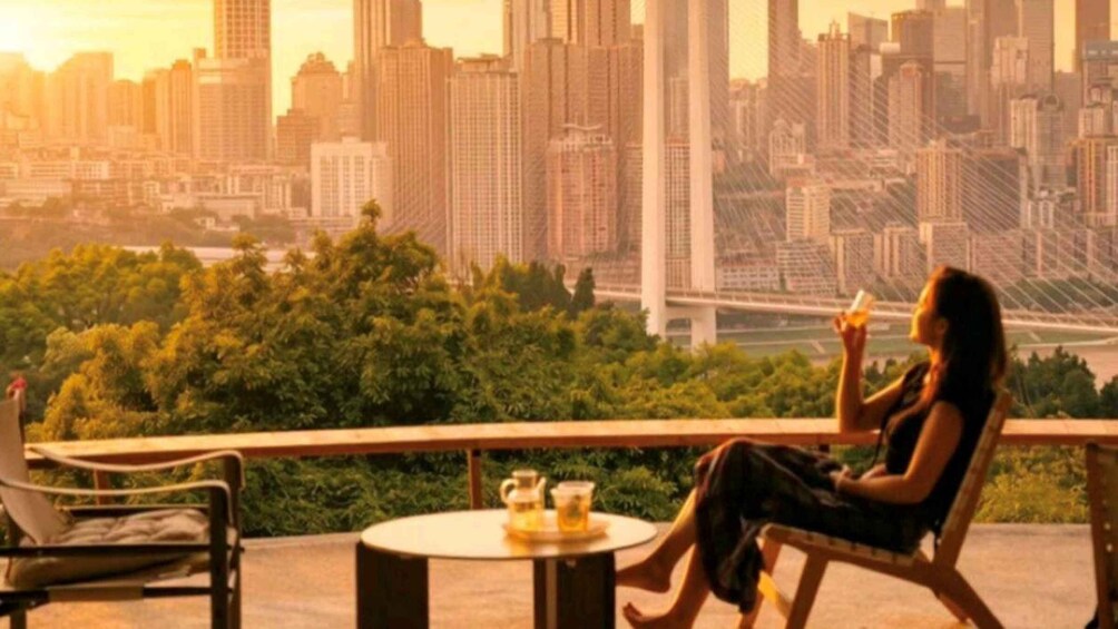 A person sitting on a balcony overlooking a cityscape with tall buildings and a bridge. 2