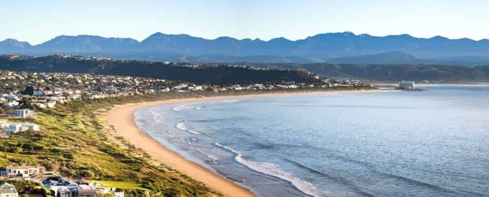A coastal landscape with a beach, houses, and mountains in the background. 3