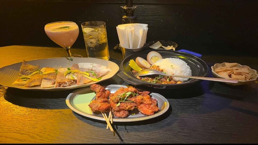 A table with various dishes, including fried fish, rice, and skewers, along with drinks and a teapot. 2