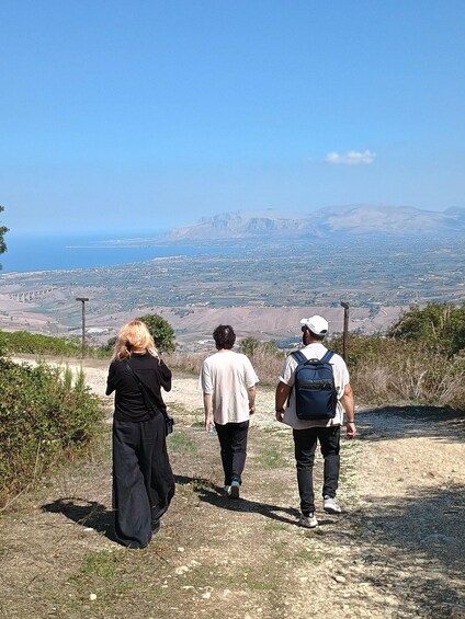 Three people walking on a dirt path with a view of a city and mountains in the distance. 2
