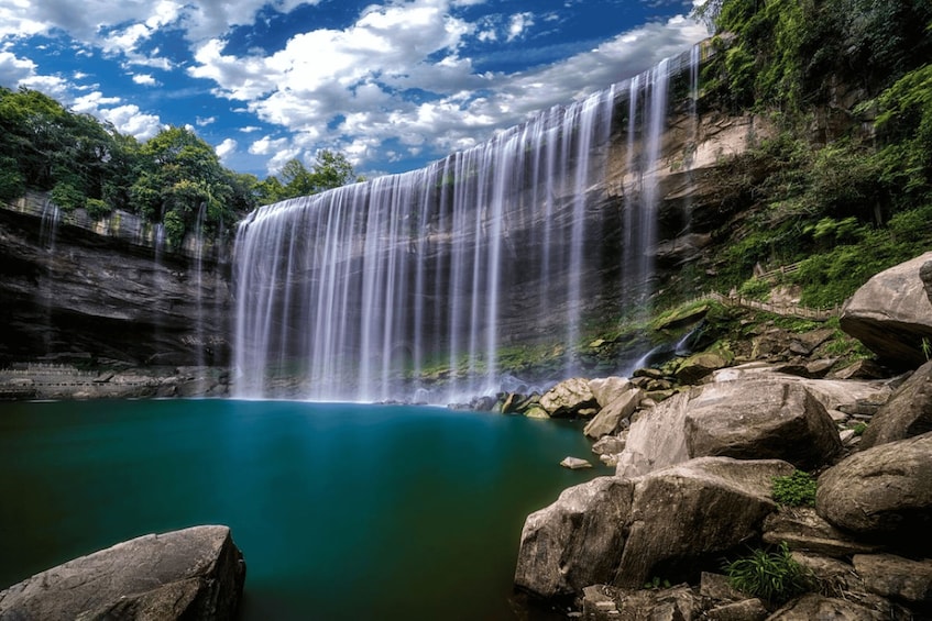 A waterfall cascading into a turquoise pool surrounded by rocks and greenery. 1