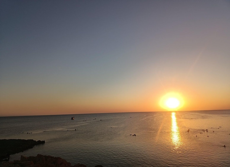 A sunset over a calm sea with boats and people. 5