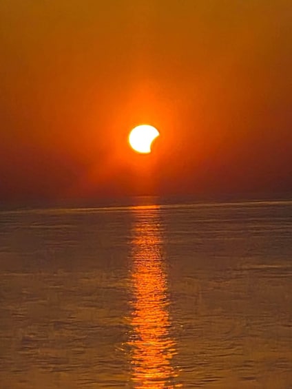 A sunset over a calm sea with a crescent moon visible. 4