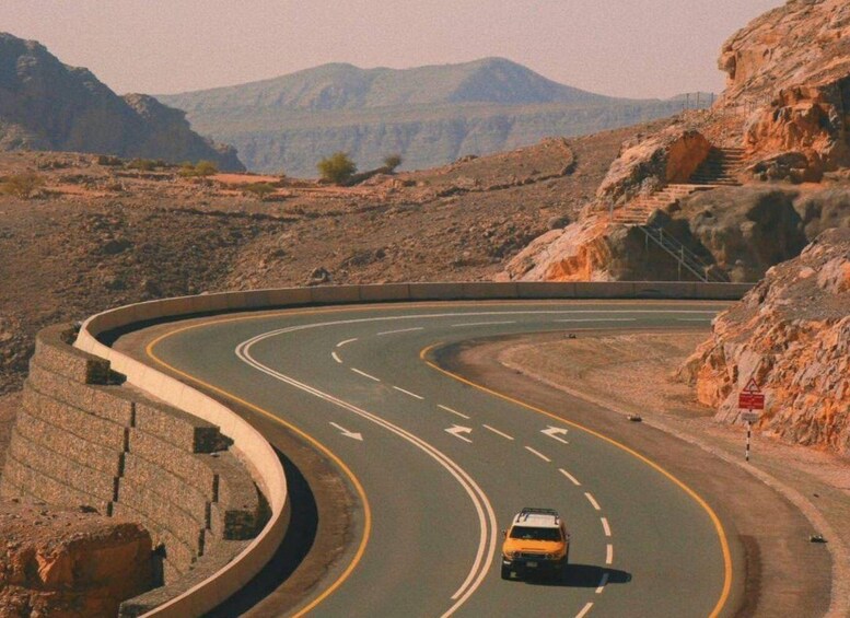 A winding road with a vehicle, surrounded by rocky terrain and mountains. 2