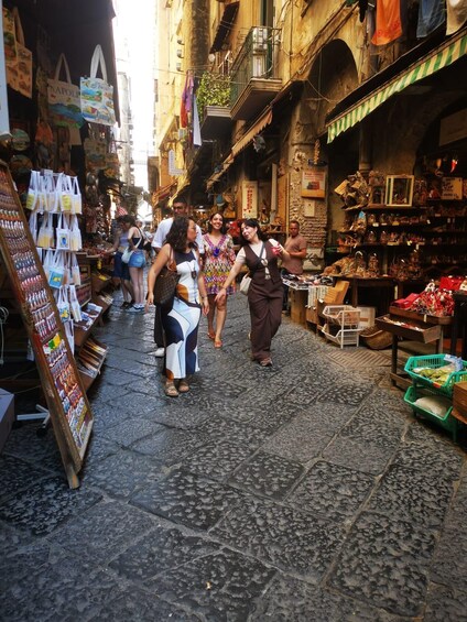 A narrow street with shops on either side, people walking, and a variety of goods displayed. 1