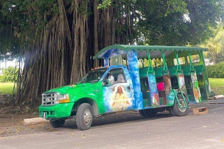 A green truck with colorful artwork parked by a large tree. 1