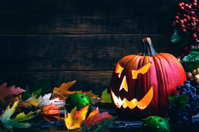 A carved pumpkin with a jack-o'-lantern face, surrounded by autumn leaves and grapes. 1
