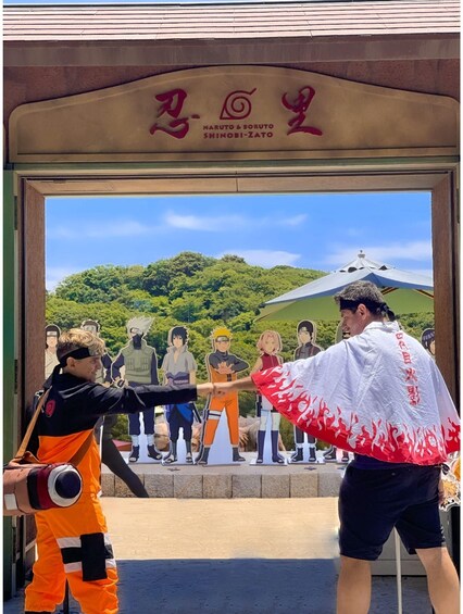 A person in an orange ninja costume holding a sword, standing in front of a building with a Naruto & Boruto sign. 1