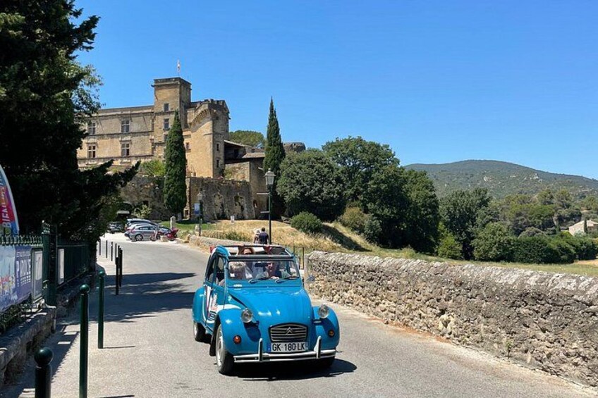 A blue vintage car driving on a road with stone walls and a castle in the background. 2