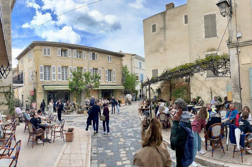 A cobblestone street with outdoor seating, people dining, and buildings with shutters. 3