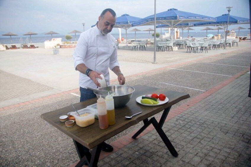 A chef preparing food outdoors with a table, a bowl, and a plate of vegetables. 1