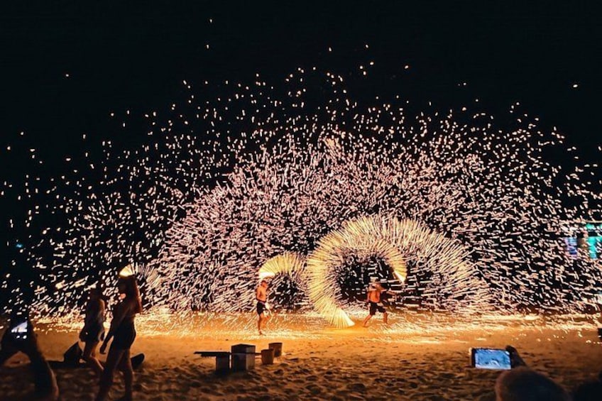 A nighttime beach scene with a large firework display creating a circular pattern on the sand. 1