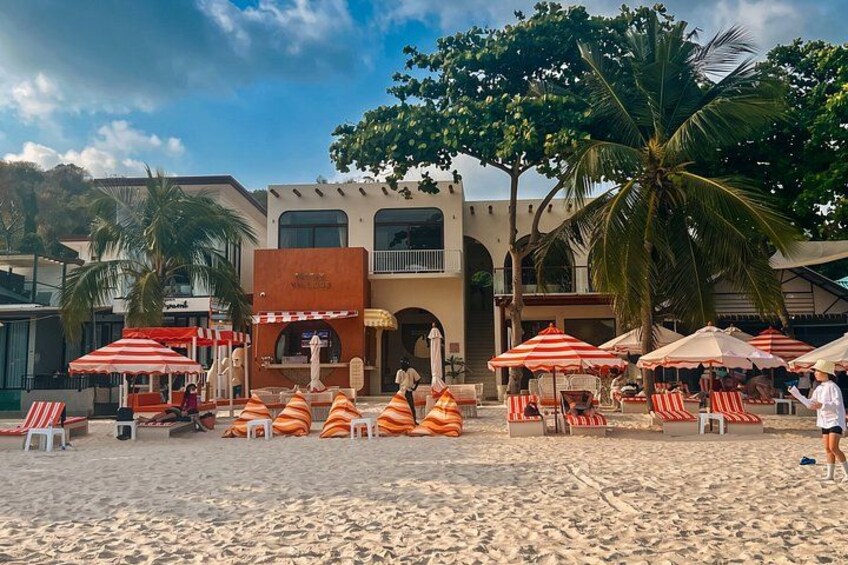 A beach with umbrellas, lounge chairs, and a building with a sign. 5