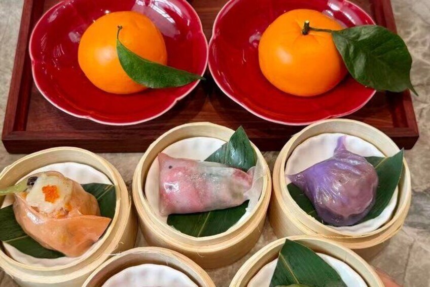A tray with two red bowls containing oranges and three bamboo containers with food items. 2