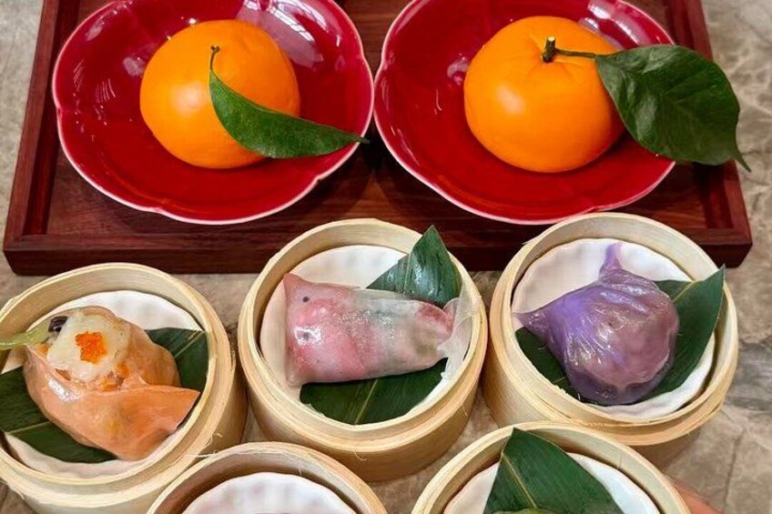 A tray with two red bowls containing oranges and three bamboo containers with food items. 2