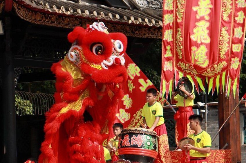 A red lion dance costume, performers in yellow, and traditional Chinese banners. 1