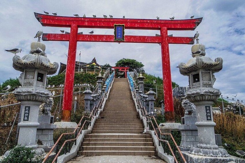 A staircase leading up to a red torii gate with stone lanterns on either side. 3