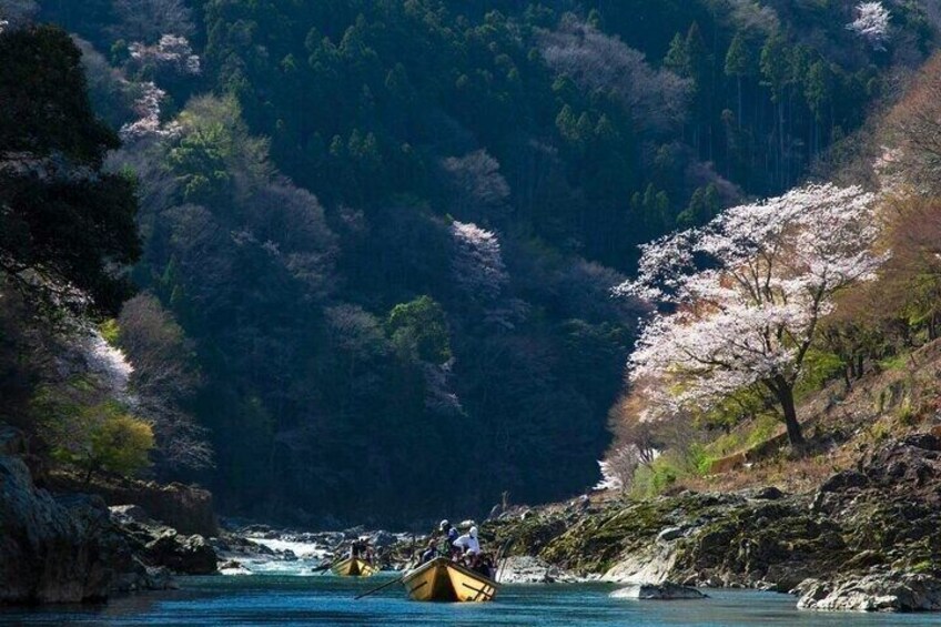 A river with boats, surrounded by forested hills and cherry blossoms. 1